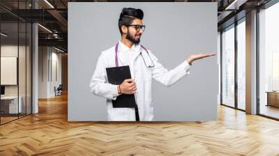 Handsome indian man doctor presenting something standing isolated over blue background Wall mural